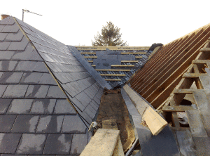 Roof construction with slate, blue underlayment, and exposed wooden framing around a central valley
