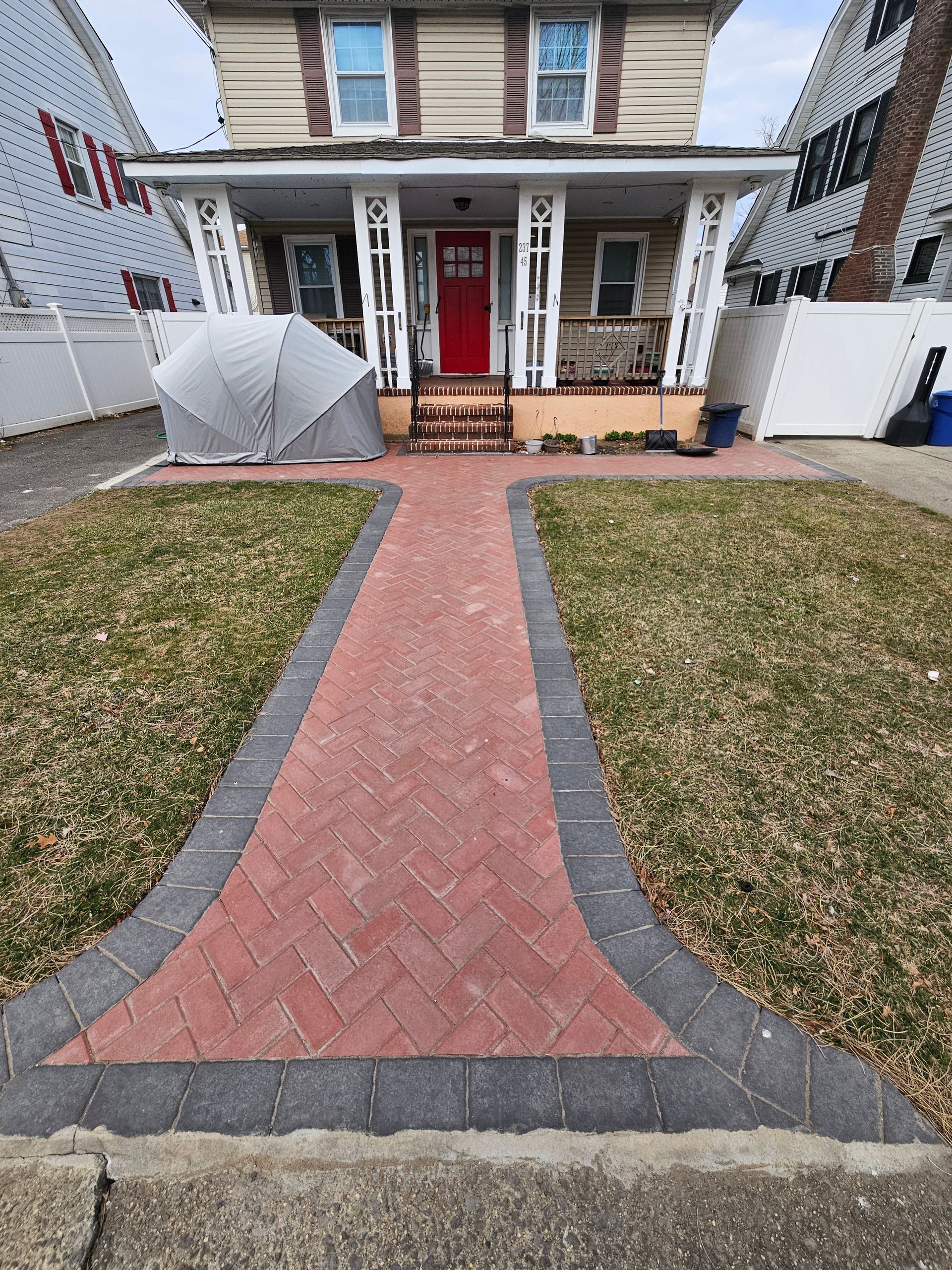 Brick pathway leading to a two-story house with a red door. Lawn on either side.