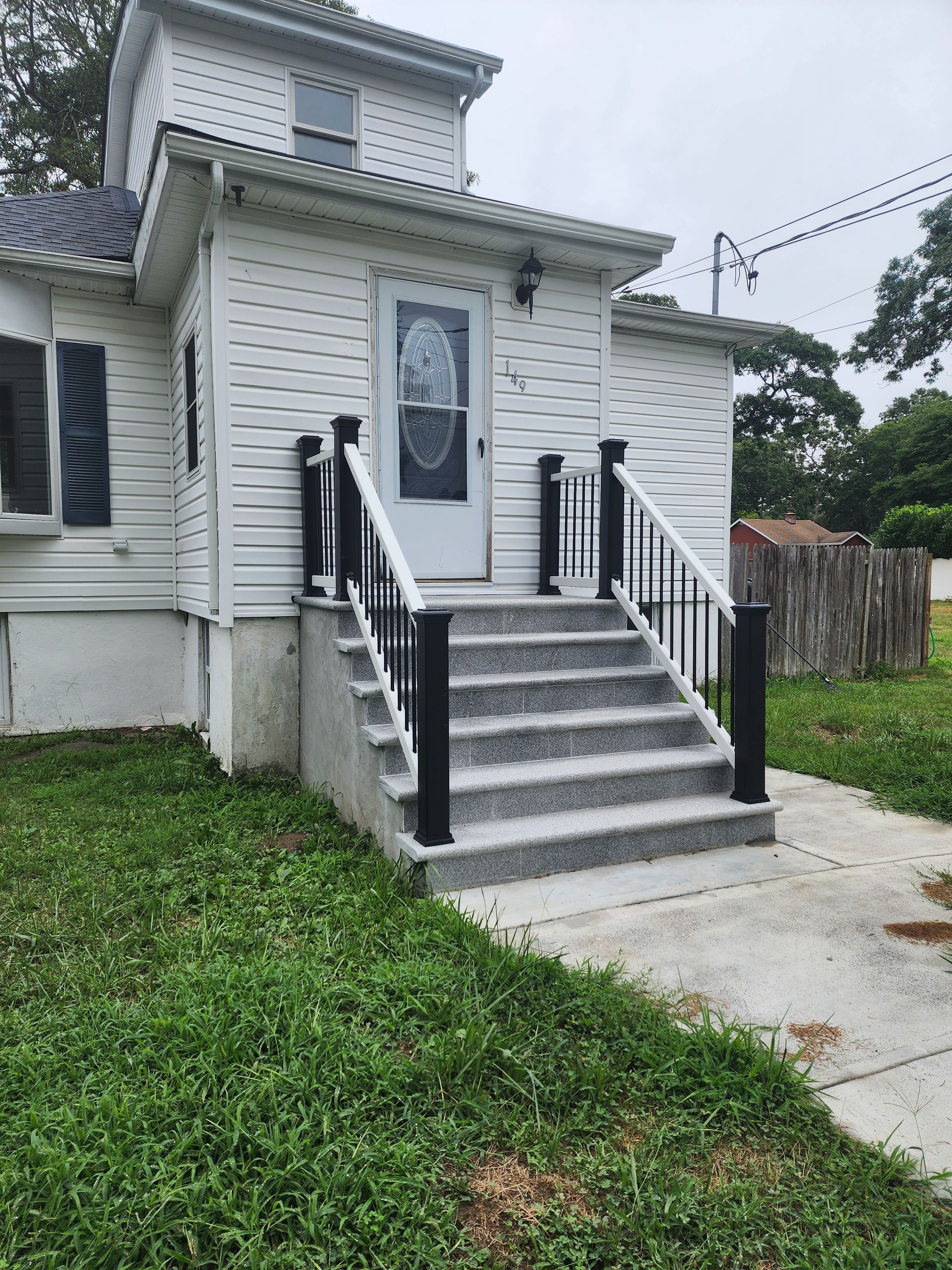 White house with steps leading to the front door. Black railings and posts on the steps. The grass is green in the foreground.
