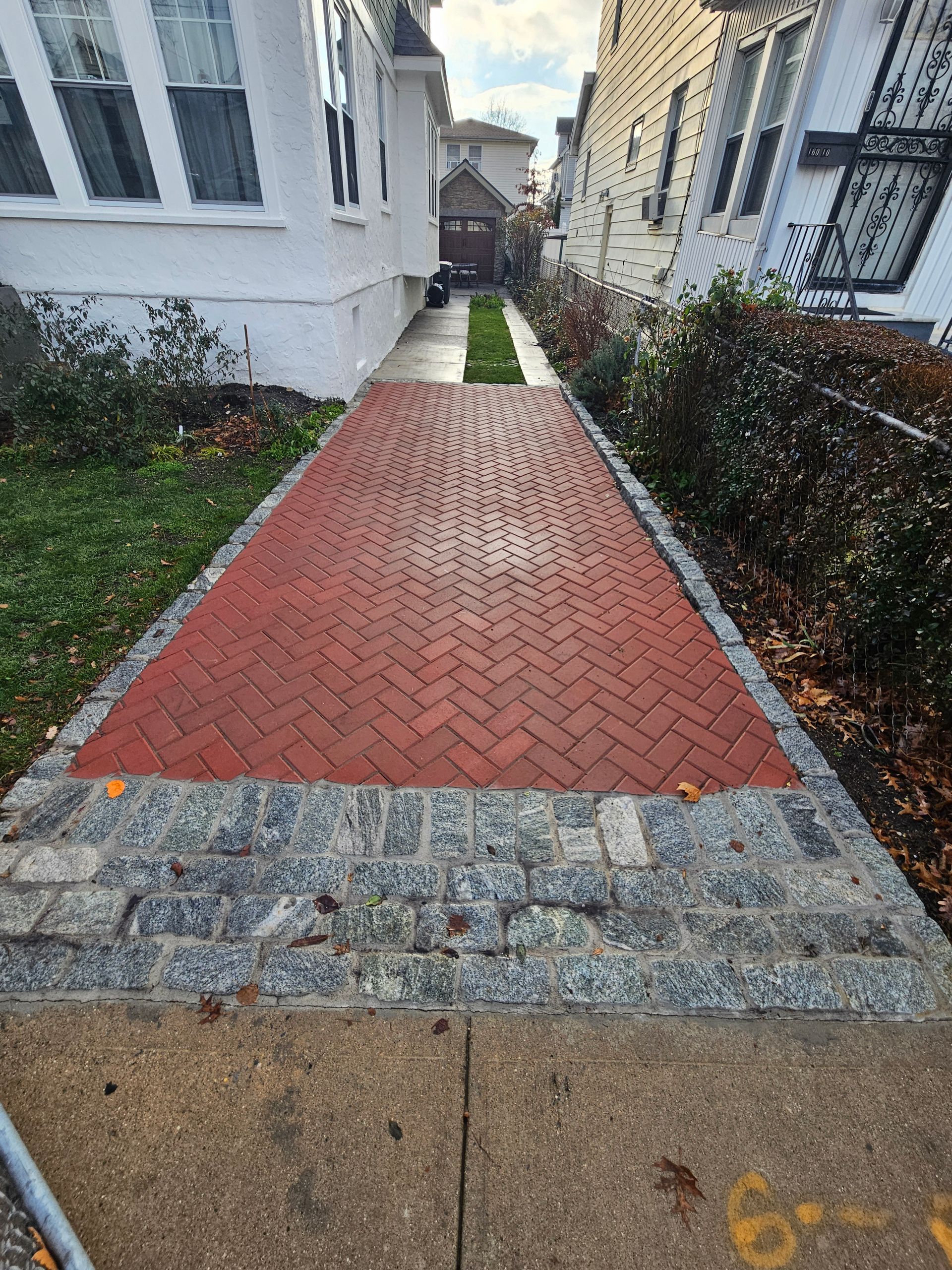 Red brick pathway between two buildings, transitioning to a gravel border and sidewalk.