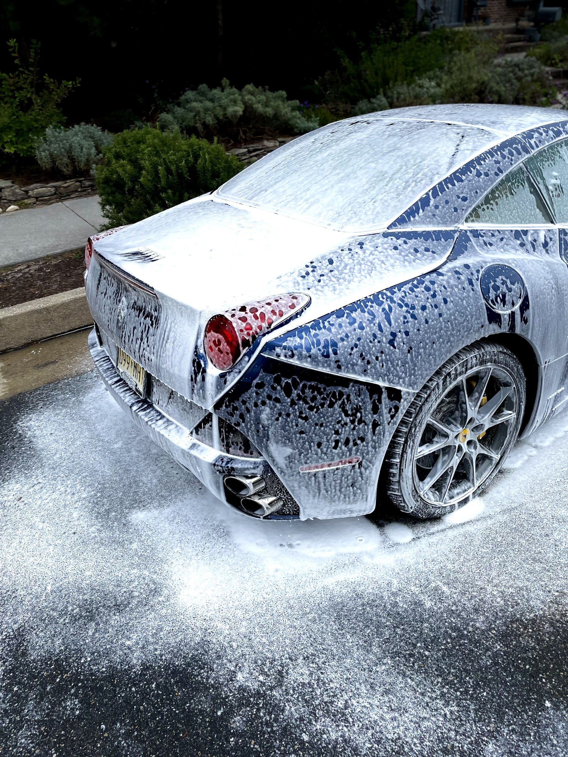 Silver sports car covered in white foam, parked on a street after washing