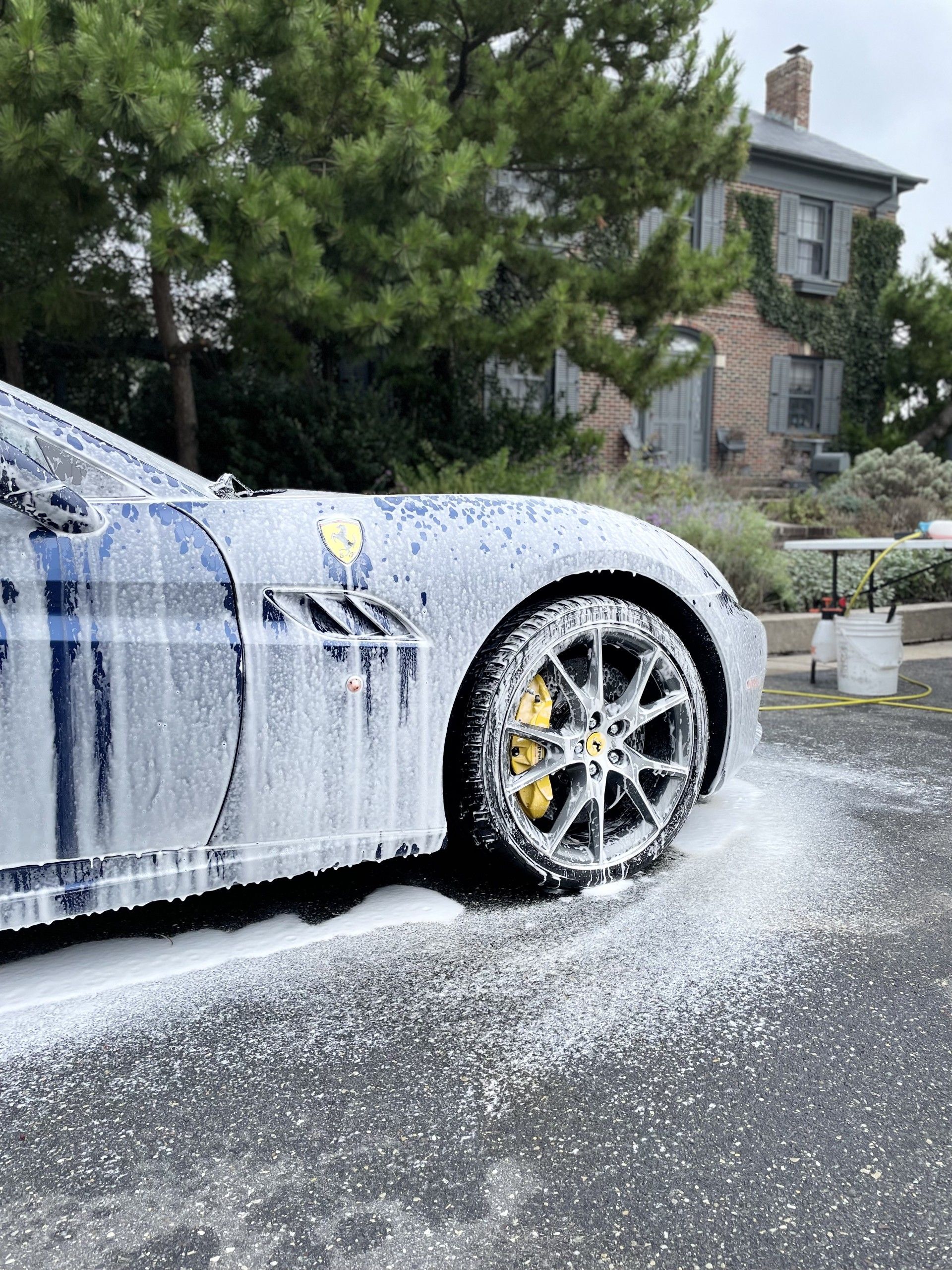 White sports car covered in foam during a driveway car wash, with soap splattered on the pavement