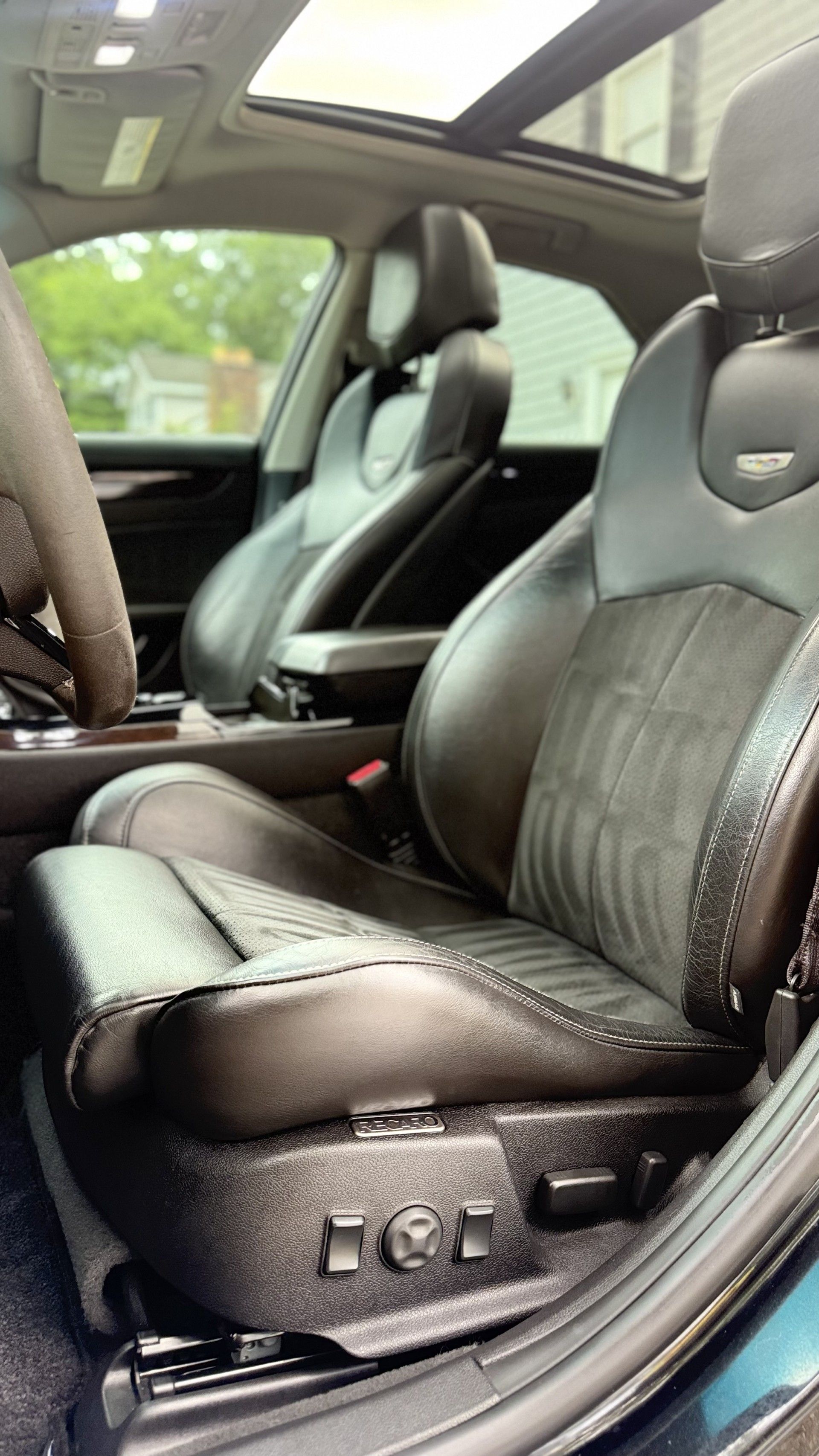 Black leather car seats inside a vehicle, viewed from the front passenger side, with a sunroof above.