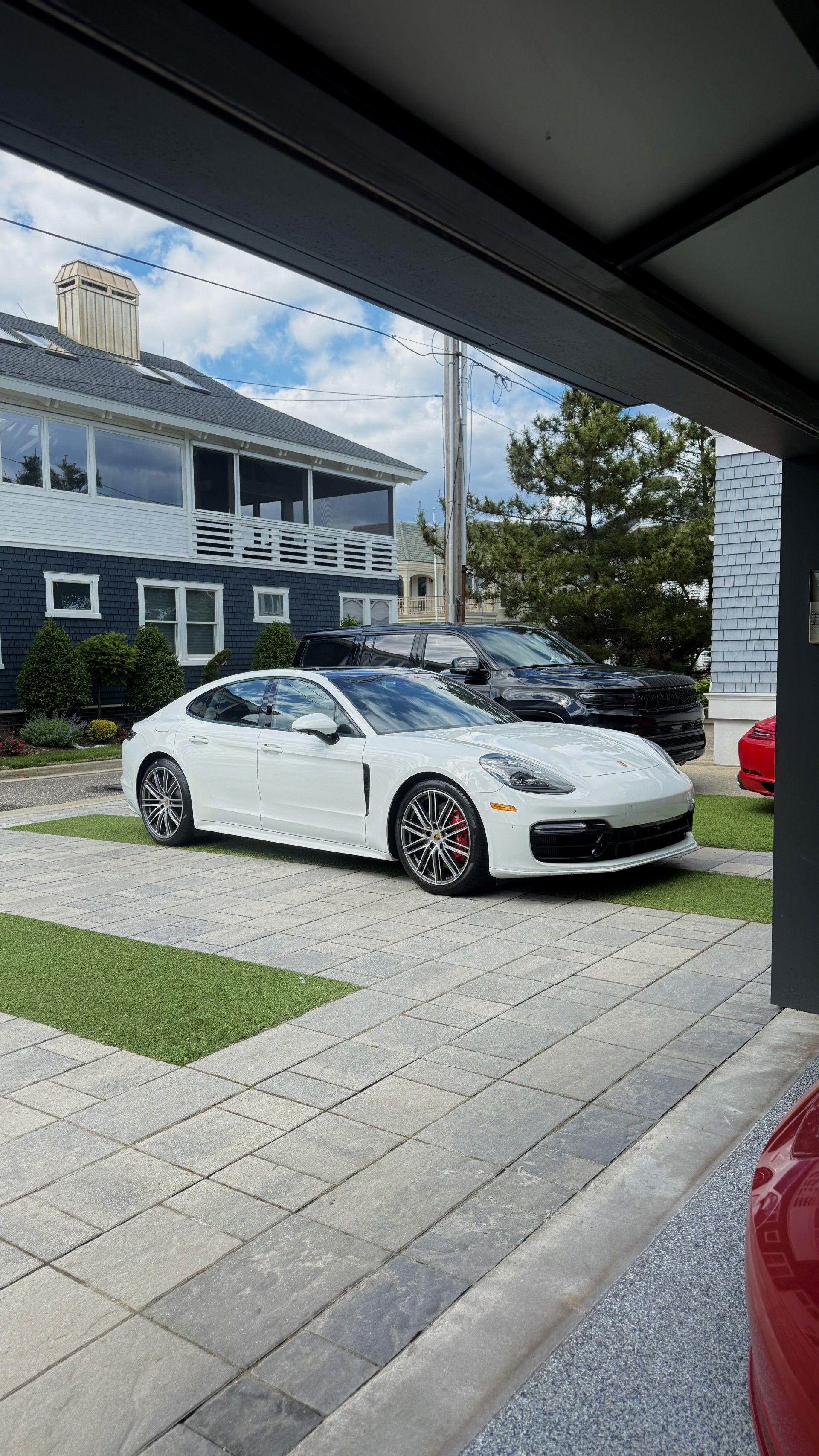 White sports car parked in a driveway beside a house, viewed from under a shaded roof.