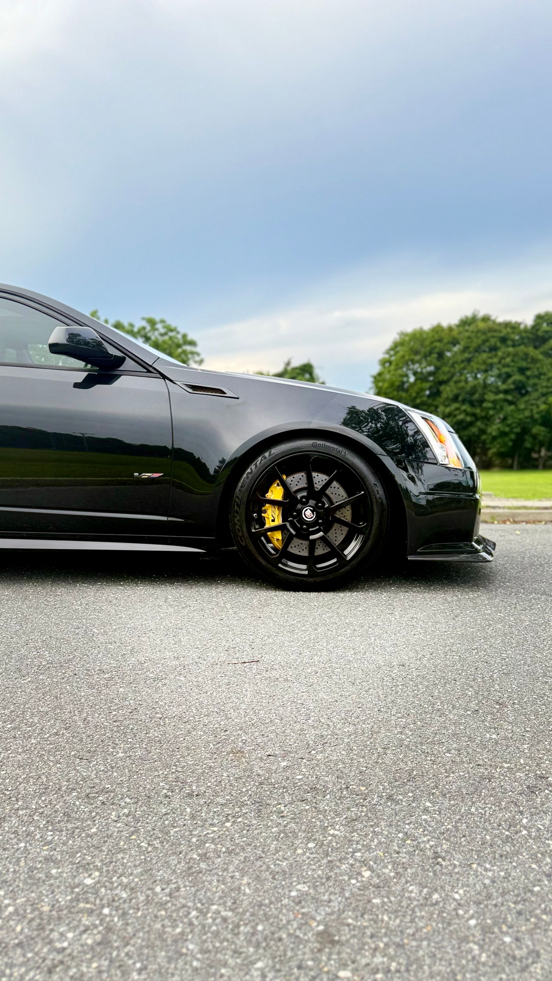 Black sports car parked on a wet road, side view with yellow brake calipers and cloudy sky.