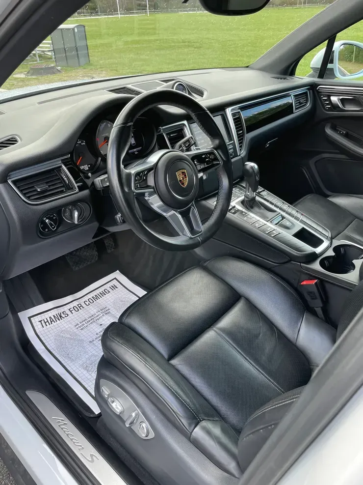 Interior of a black Porsche sports car, showing the driver's seat, steering wheel, and center console.