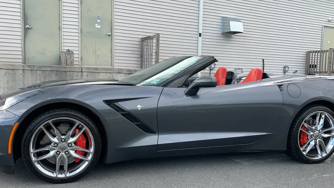 Black convertible sports car with red seats parked beside a building and wall lattice.