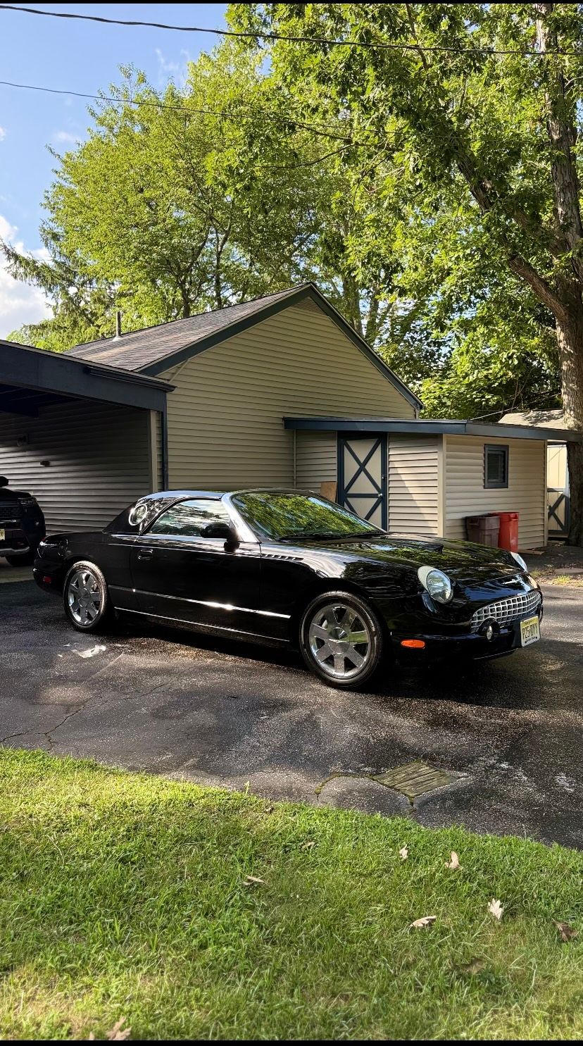 Black convertible parked in a driveway beside a garage and house under trees.