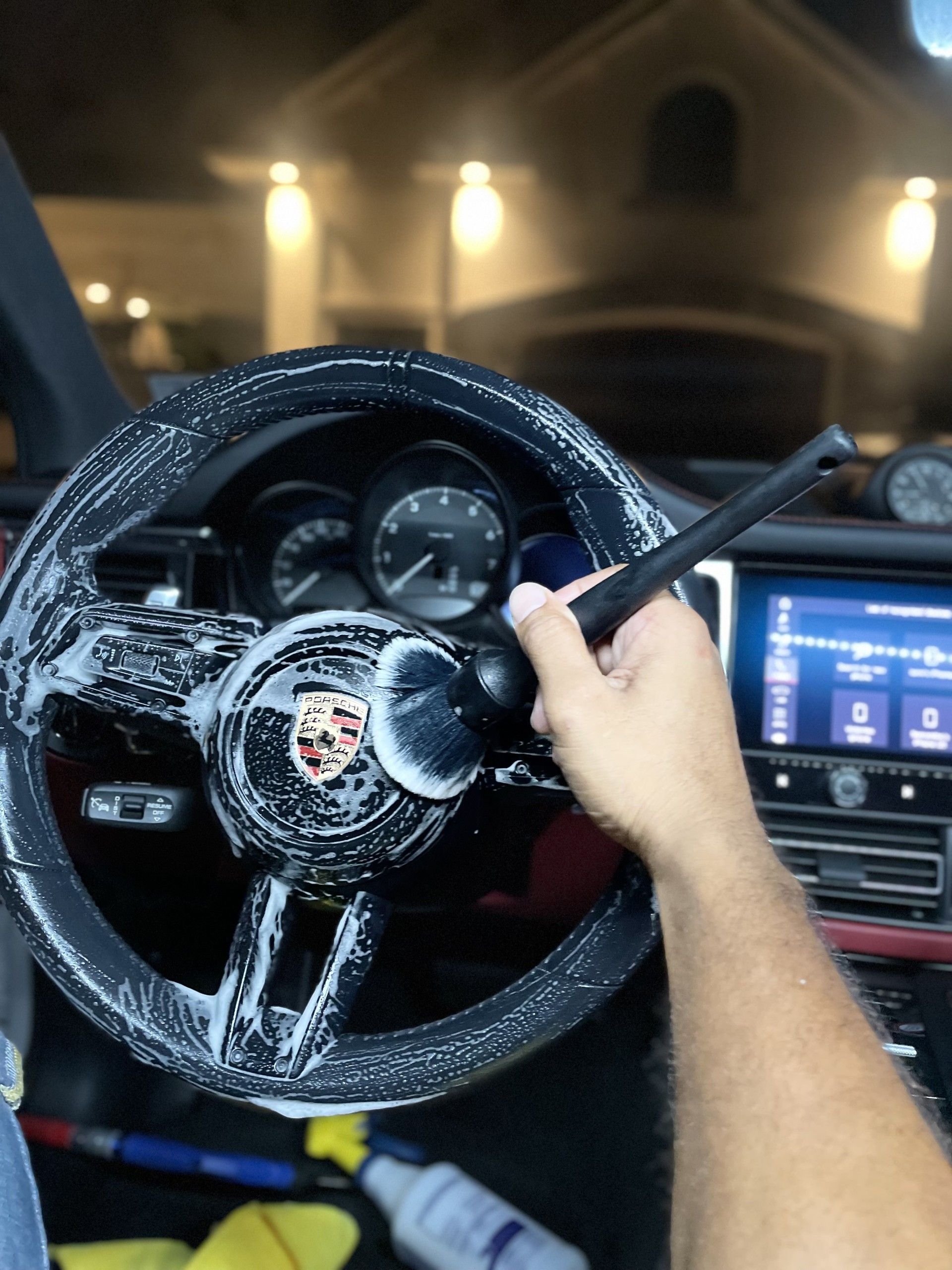 Driver cleaning a snow-covered Porsche steering wheel inside a car at night.