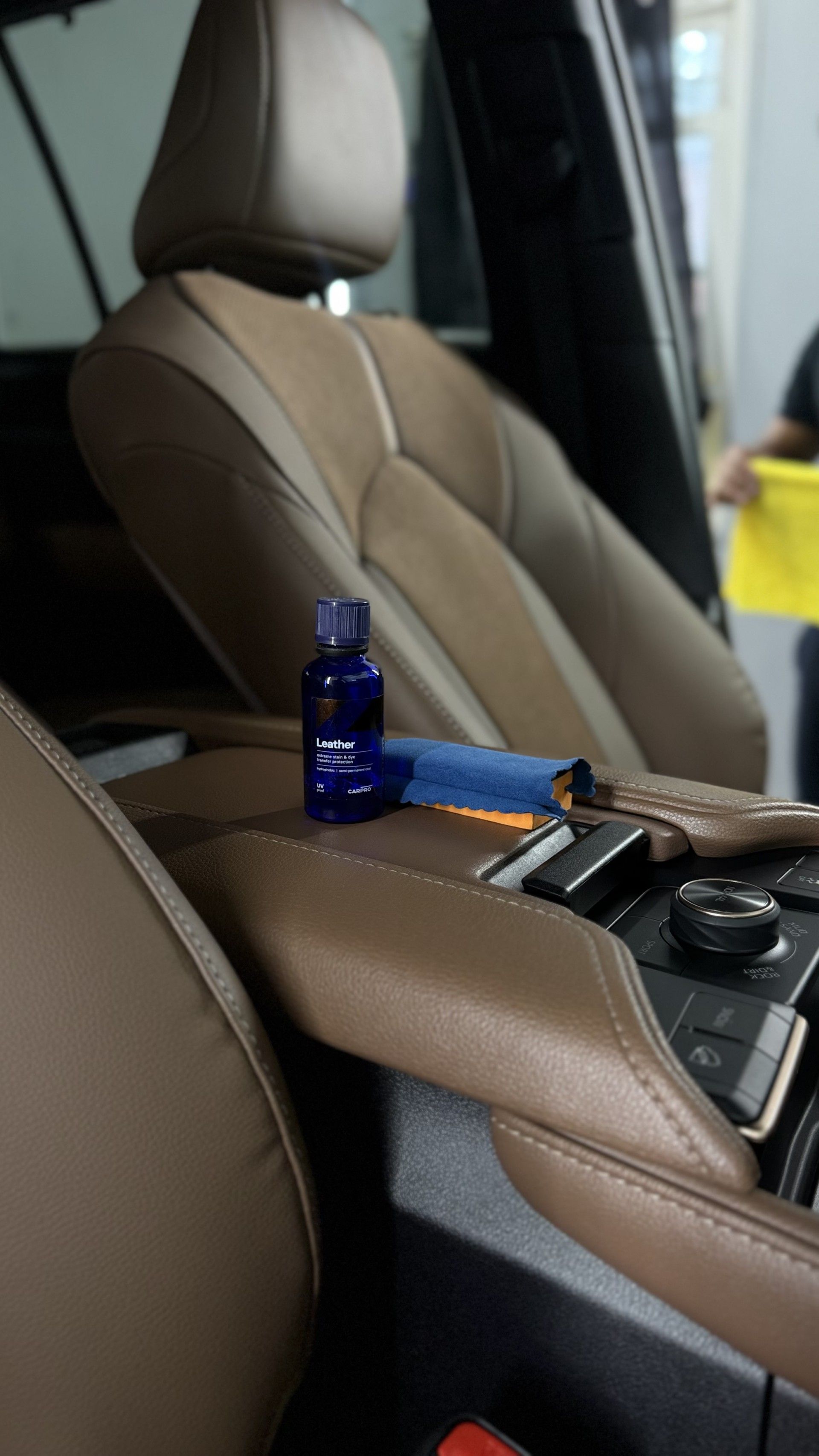 Car interior with a brown leather seat and center console holding a blue bottle and a small tool.