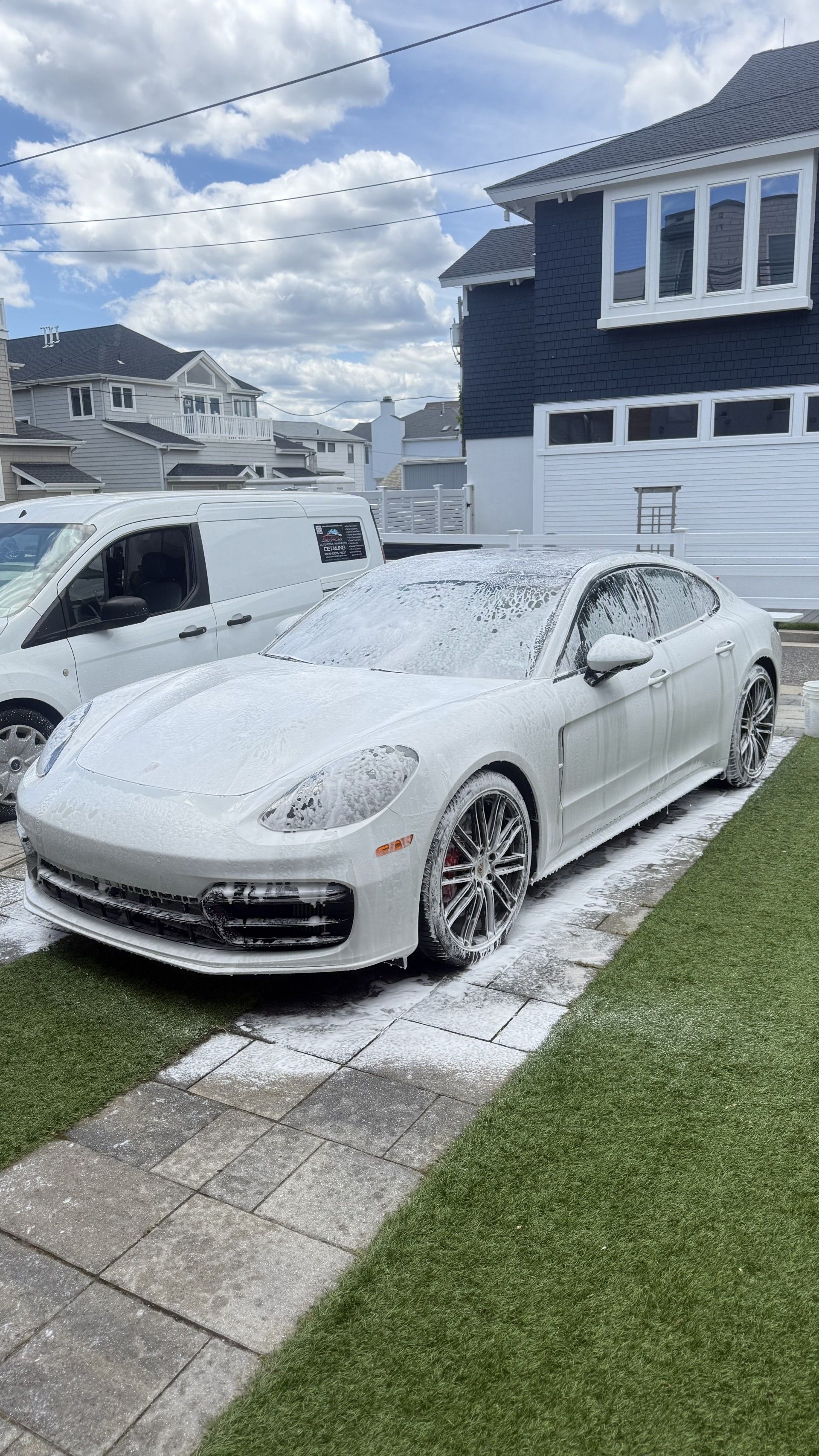 White sports car parked in a snowy suburban driveway beside a white van and house