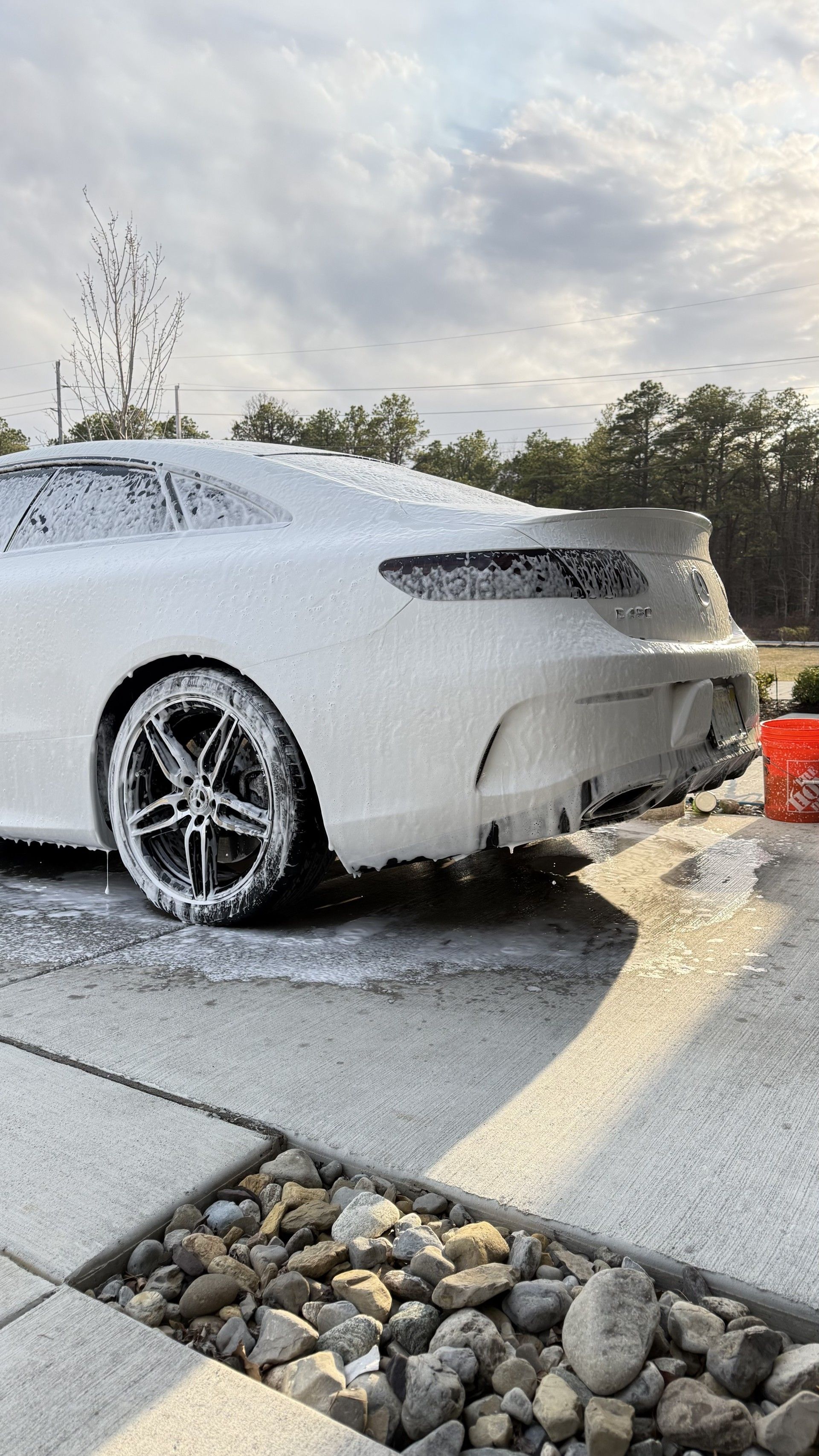 White sports car covered in foam at a self-service car wash, rear view with wet pavement and soap runoff