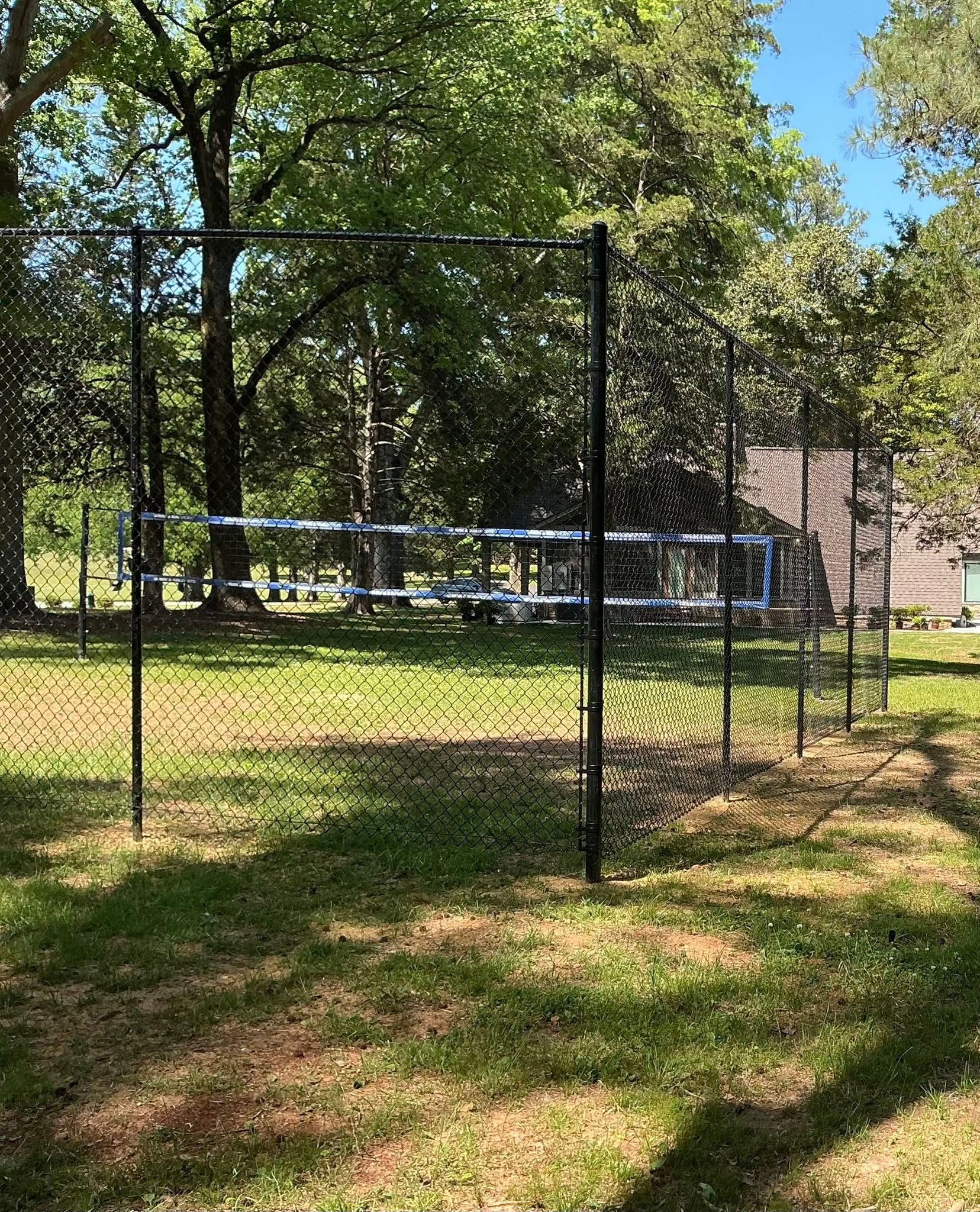 Chain-link fence around a grassy park with a blue trampoline or pool frame under trees.
