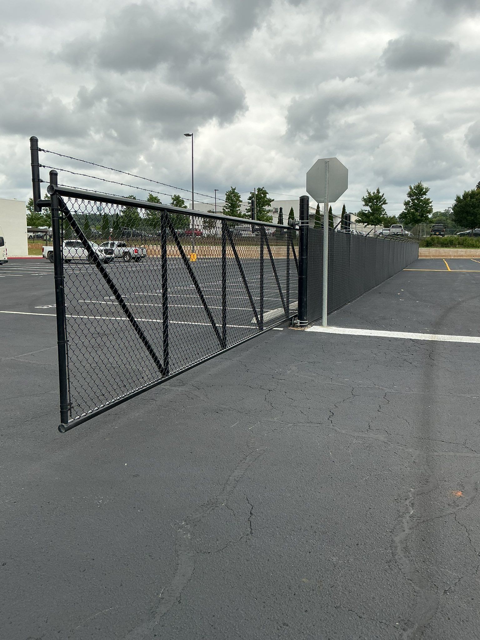 Black chain-link gate along a fenced asphalt lot under a cloudy sky