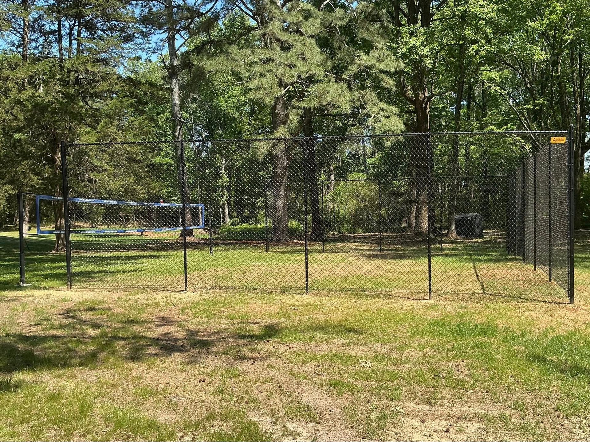 Chain-link fence around a grassy yard with trees in the background.