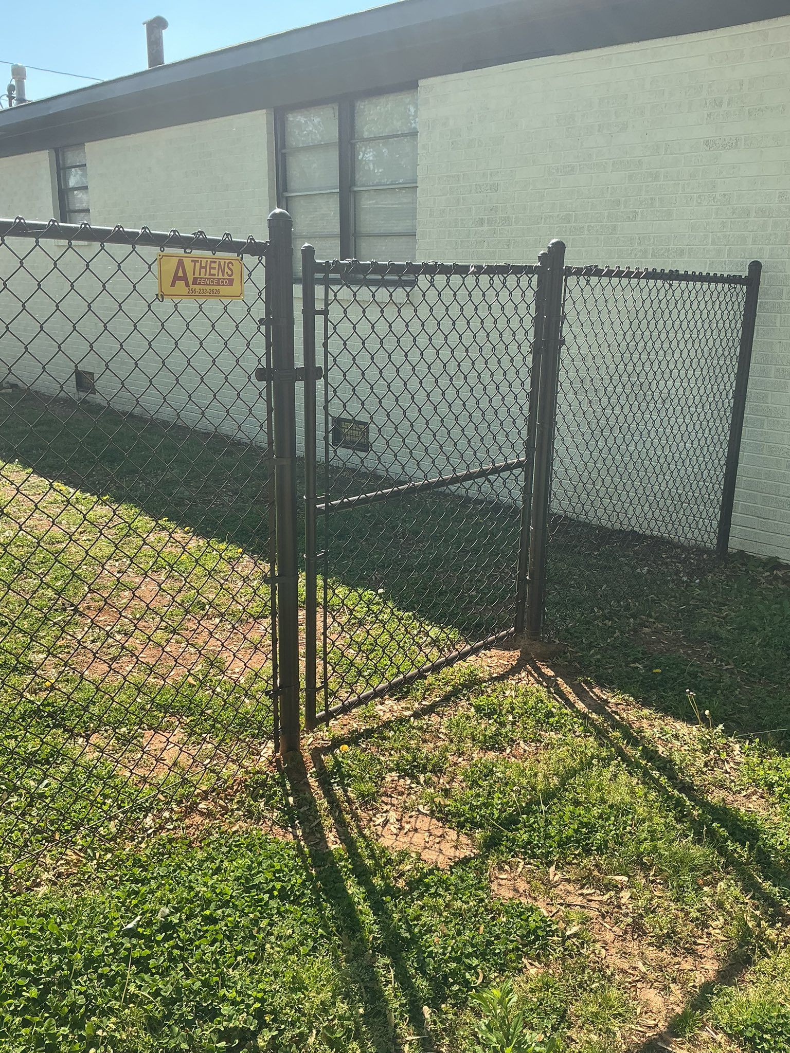 Chain-link fence gate beside a white building, with an “ALARM” sign on the fence.