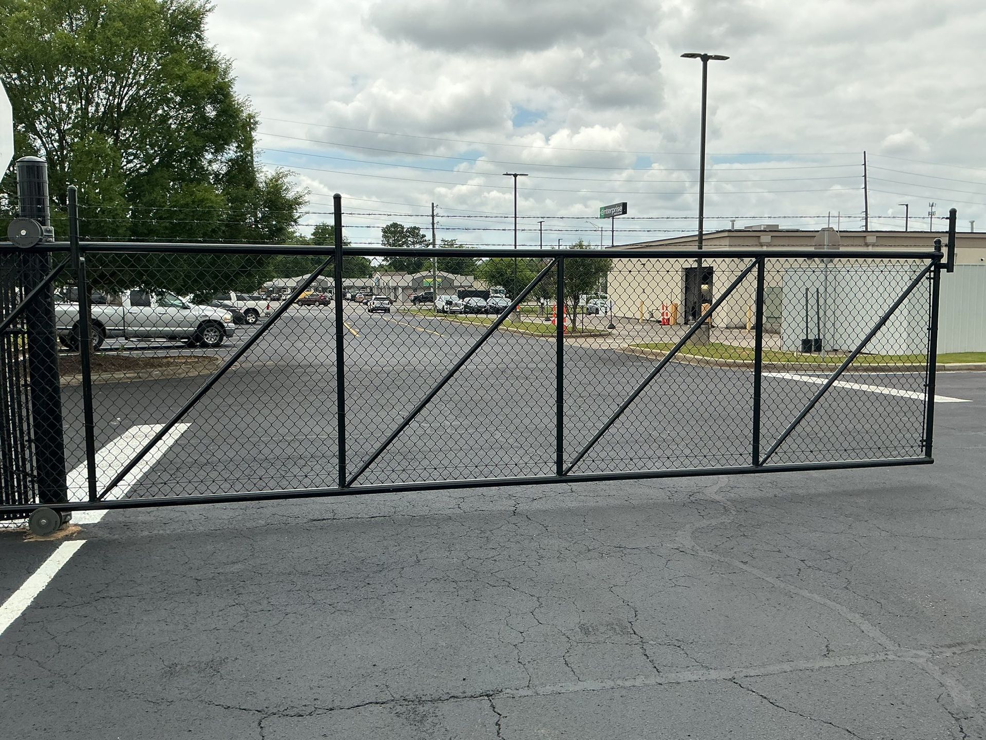 Black chain-link gate across a paved parking lot under a cloudy sky