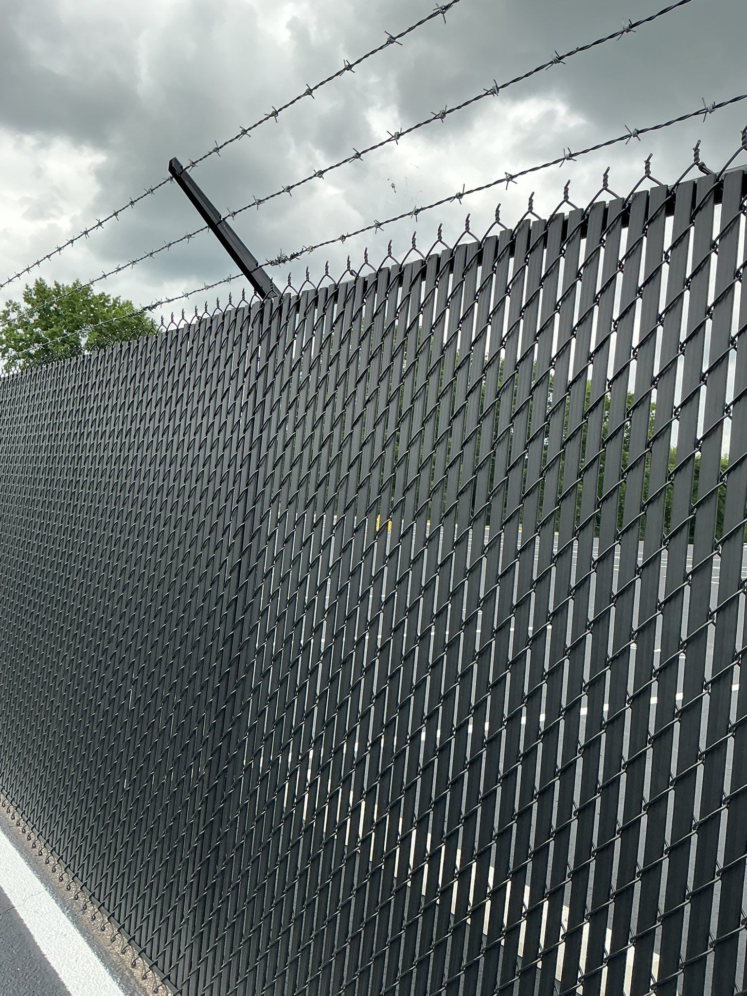 Chain-link fence with barbed wire along a roadside under a cloudy sky