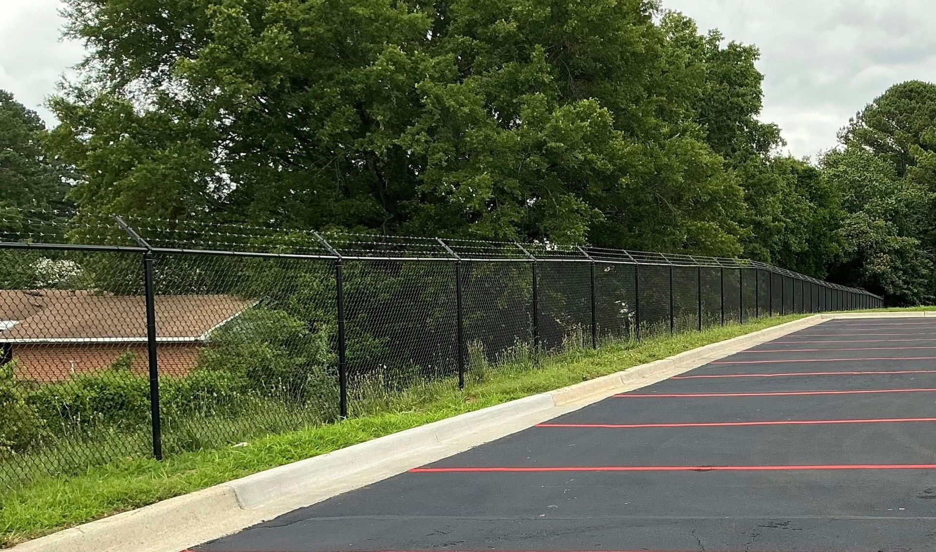 Empty paved lot beside a chain-link fence and trees on a cloudy day