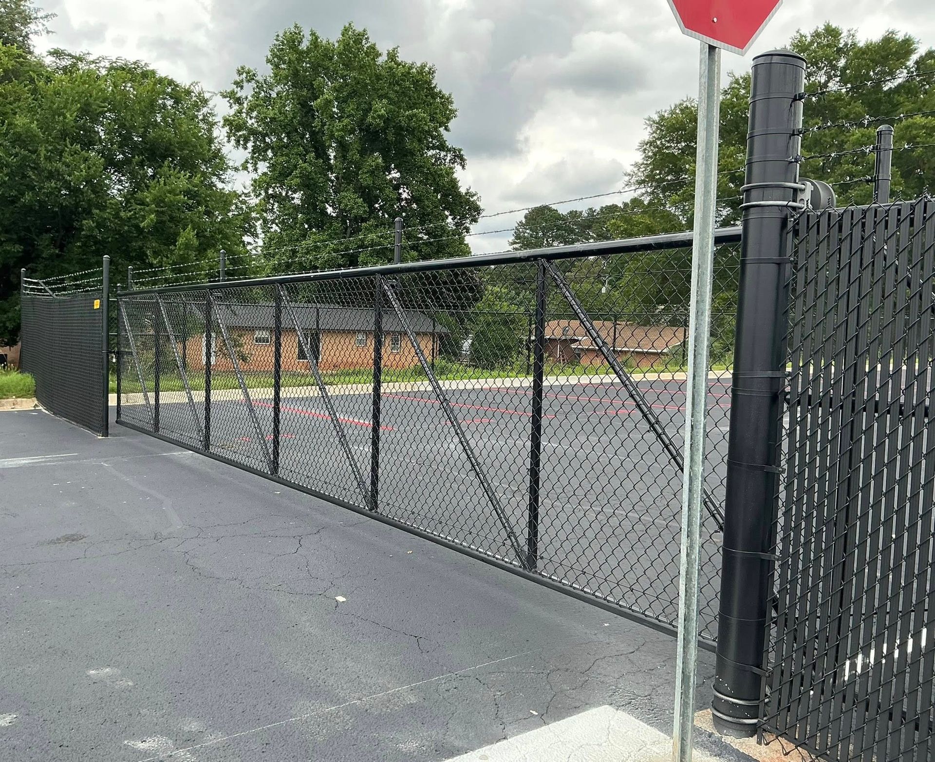 Chain-link gate beside a paved path, with a stop sign and trees in the background.