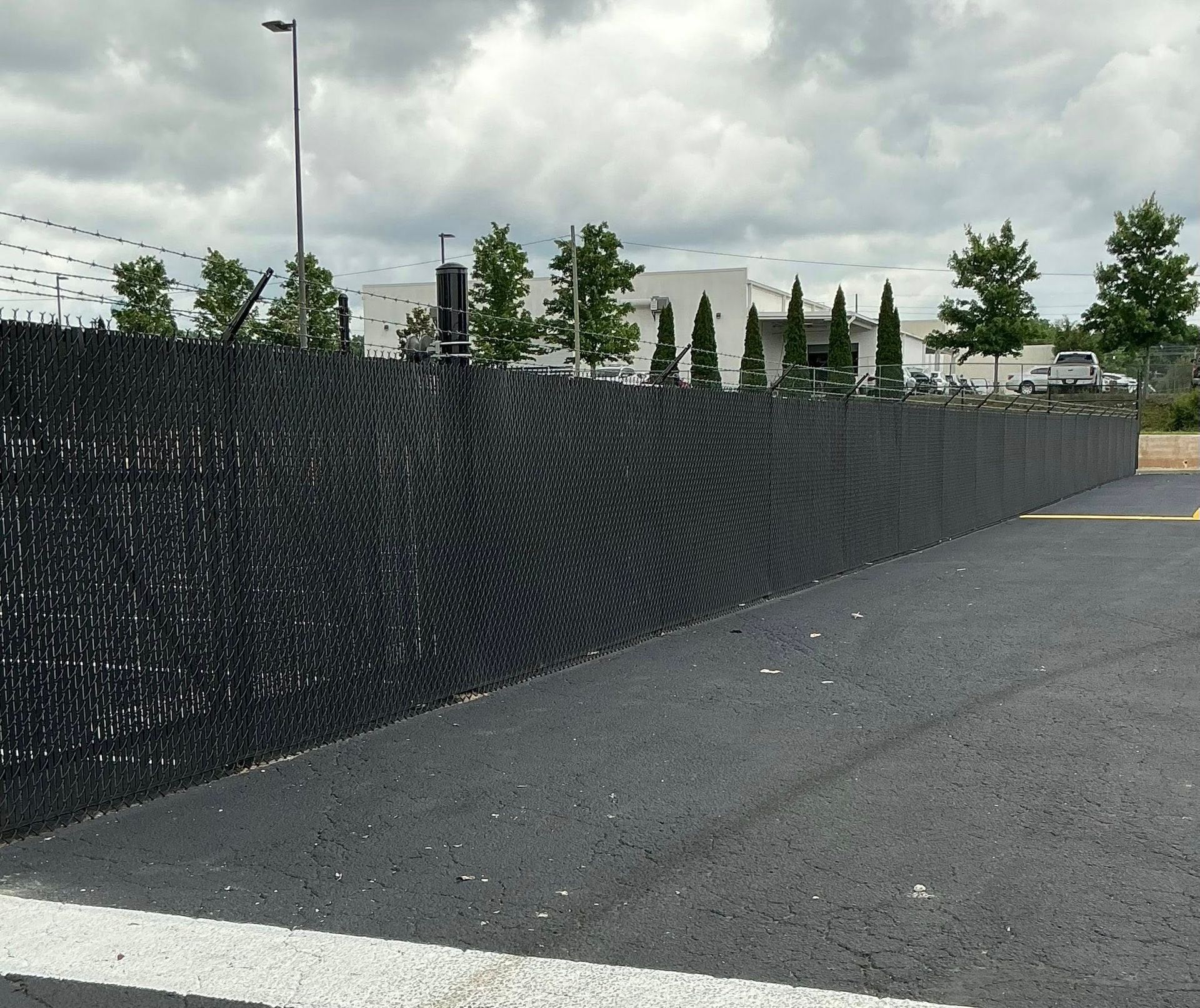 Long black chain-link fence beside an empty paved lot under cloudy skies.