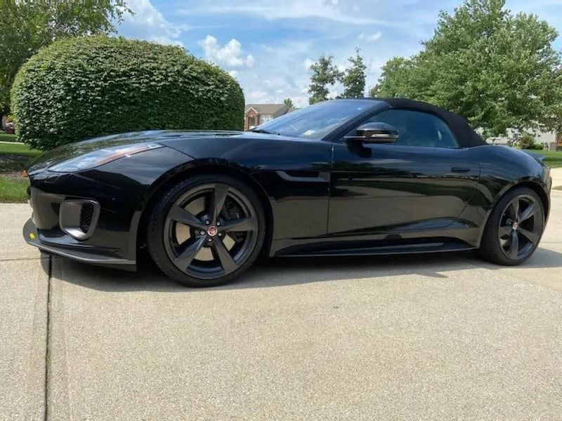 Black Jaguar F-Type convertible parked on a driveway with the top down on a sunny day.