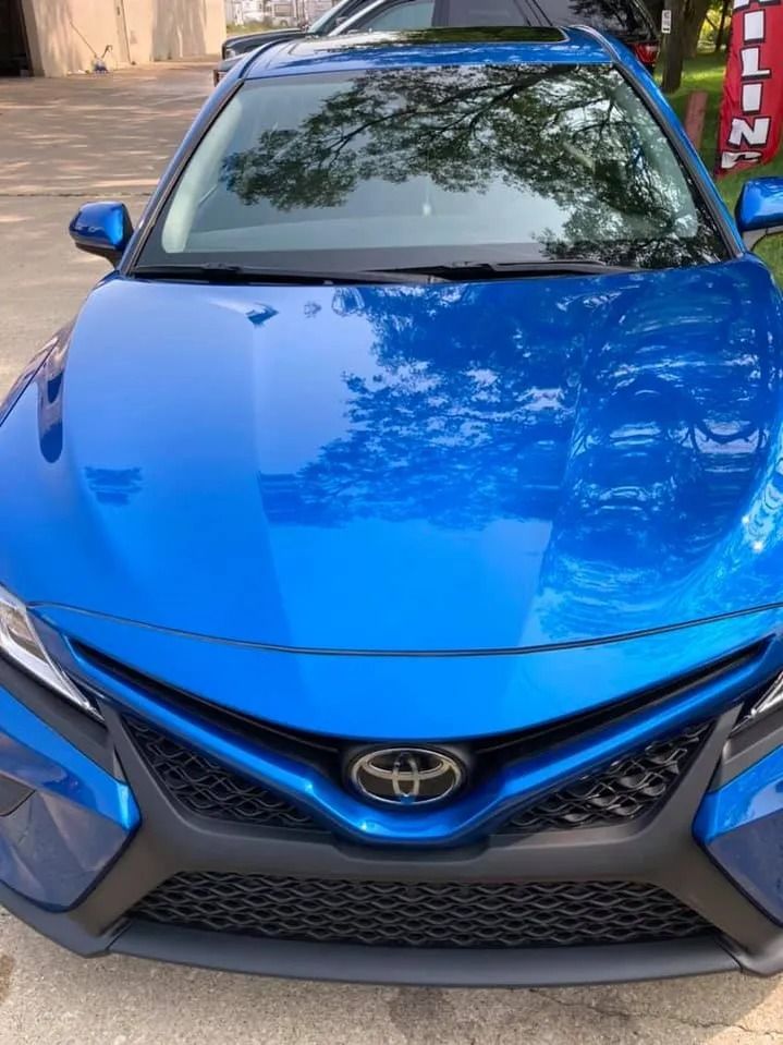 Blue Toyota Camry, front view, with the Toyota emblem in the center of the grille.