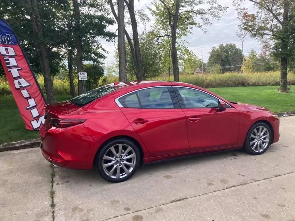 Red Mazda sedan parked on concrete, advertising flag in the background.
