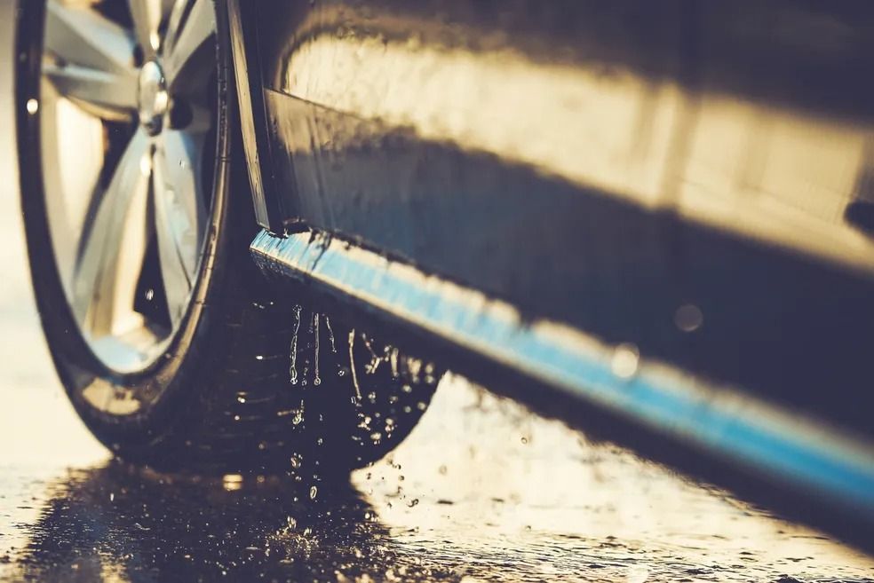 Close-up of a car tire splashing water on a wet road, highlighting motion and wet conditions.