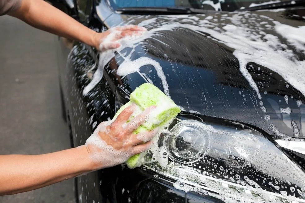 Person washing a black car with soapy sponge.