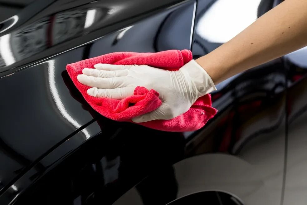Gloved hand wiping a red cloth on a shiny, black car, likely polishing the surface.