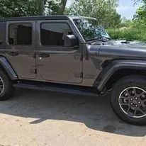 Dark gray Jeep SUV parked on a paved surface near greenery.