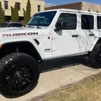 White Jeep Rubicon with black wheels parked outdoors.