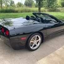 Black convertible sports car parked on a paved surface near green grass.