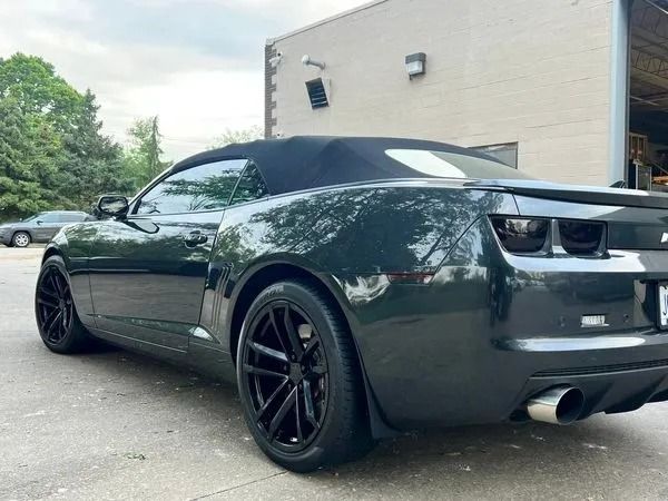 Black convertible car with black wheels parked near a building.