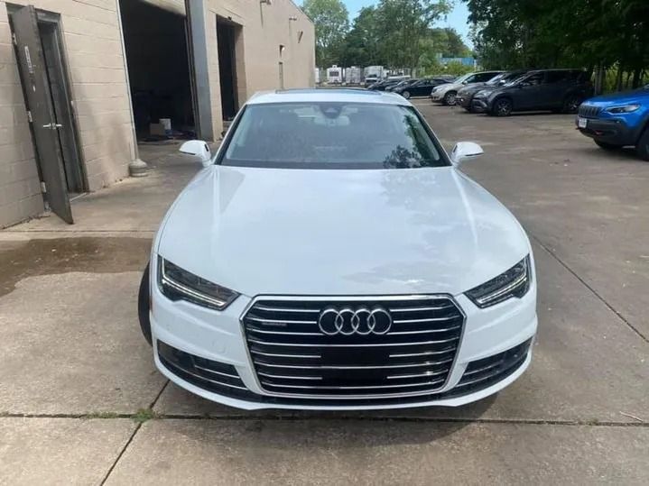 White Audi A7 parked outside a building with a gray concrete surface, sunny day.