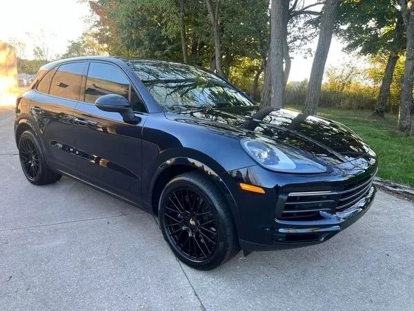 Dark blue Porsche SUV parked on pavement, with black wheels. Trees in the background.