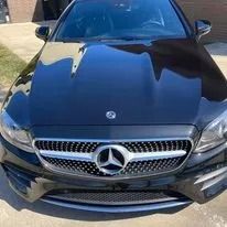 Black Mercedes-Benz sedan, front view, shiny finish, silver emblem on grill.
