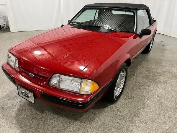 Red Ford Mustang convertible with black top, parked indoors.
