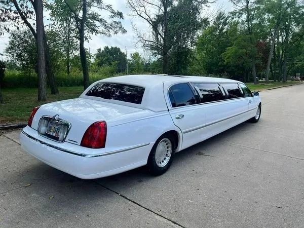 White limousine on a paved road, trees in the background.