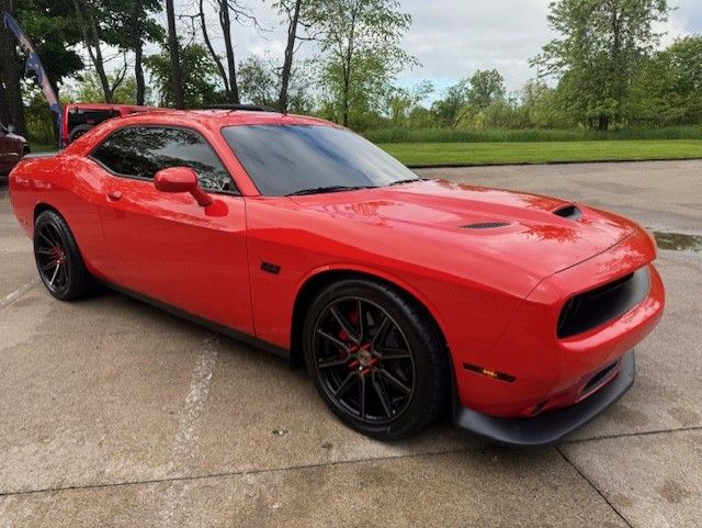 Red Dodge Challenger sports car on a concrete surface with tinted windows and black wheels.