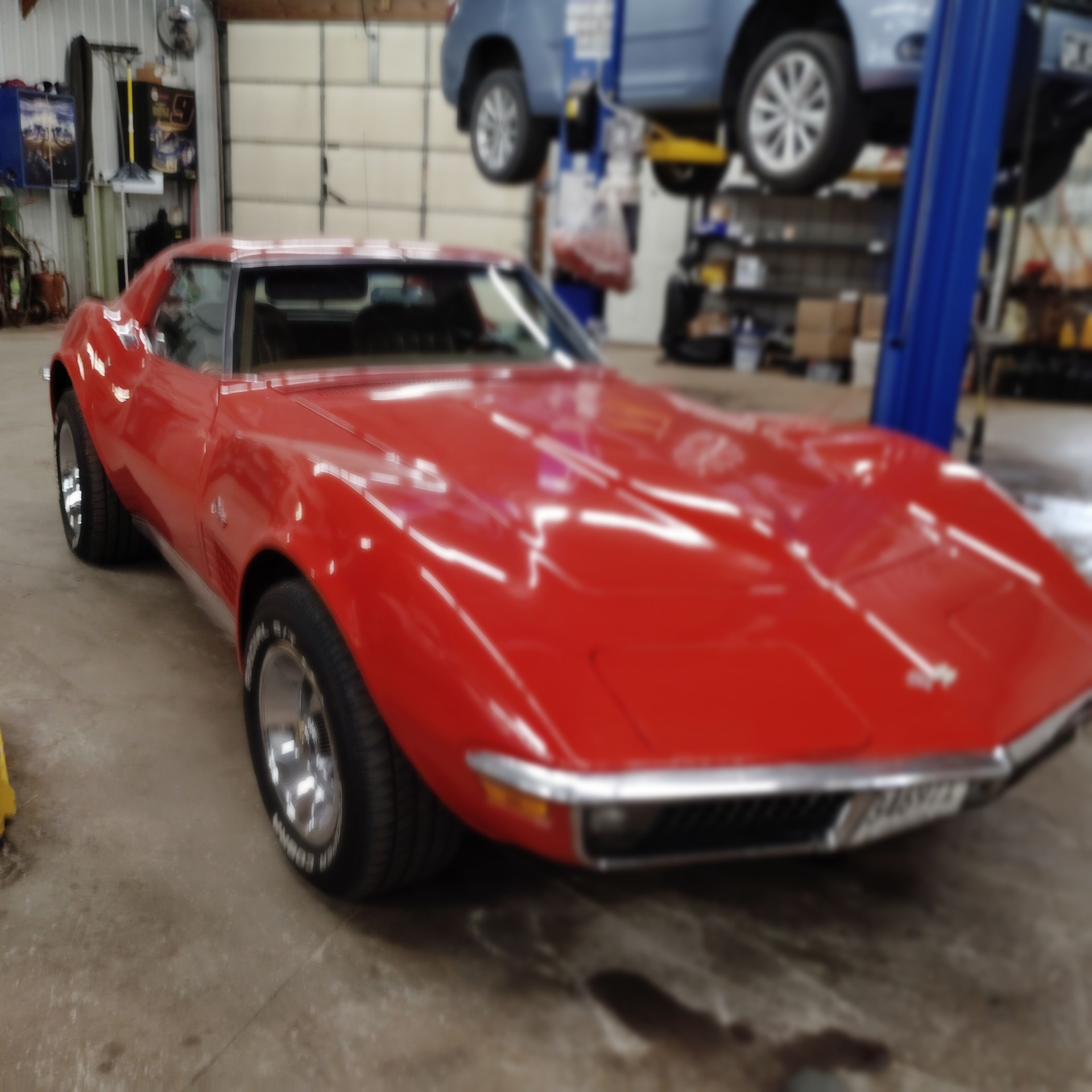 Red classic sports car in a garage, with a blue SUV lifted on a rack in the background.