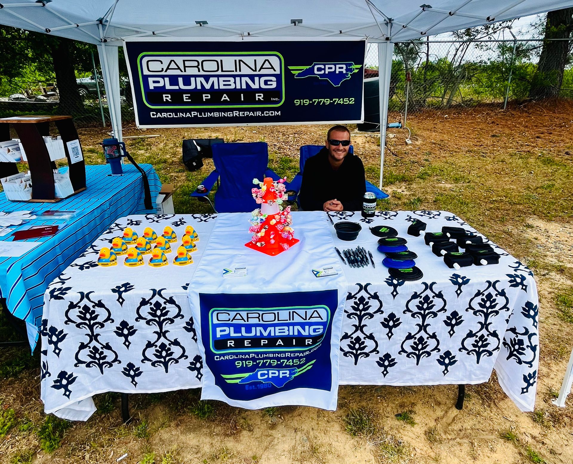 A man sits at a table under a carolina plumbing sign