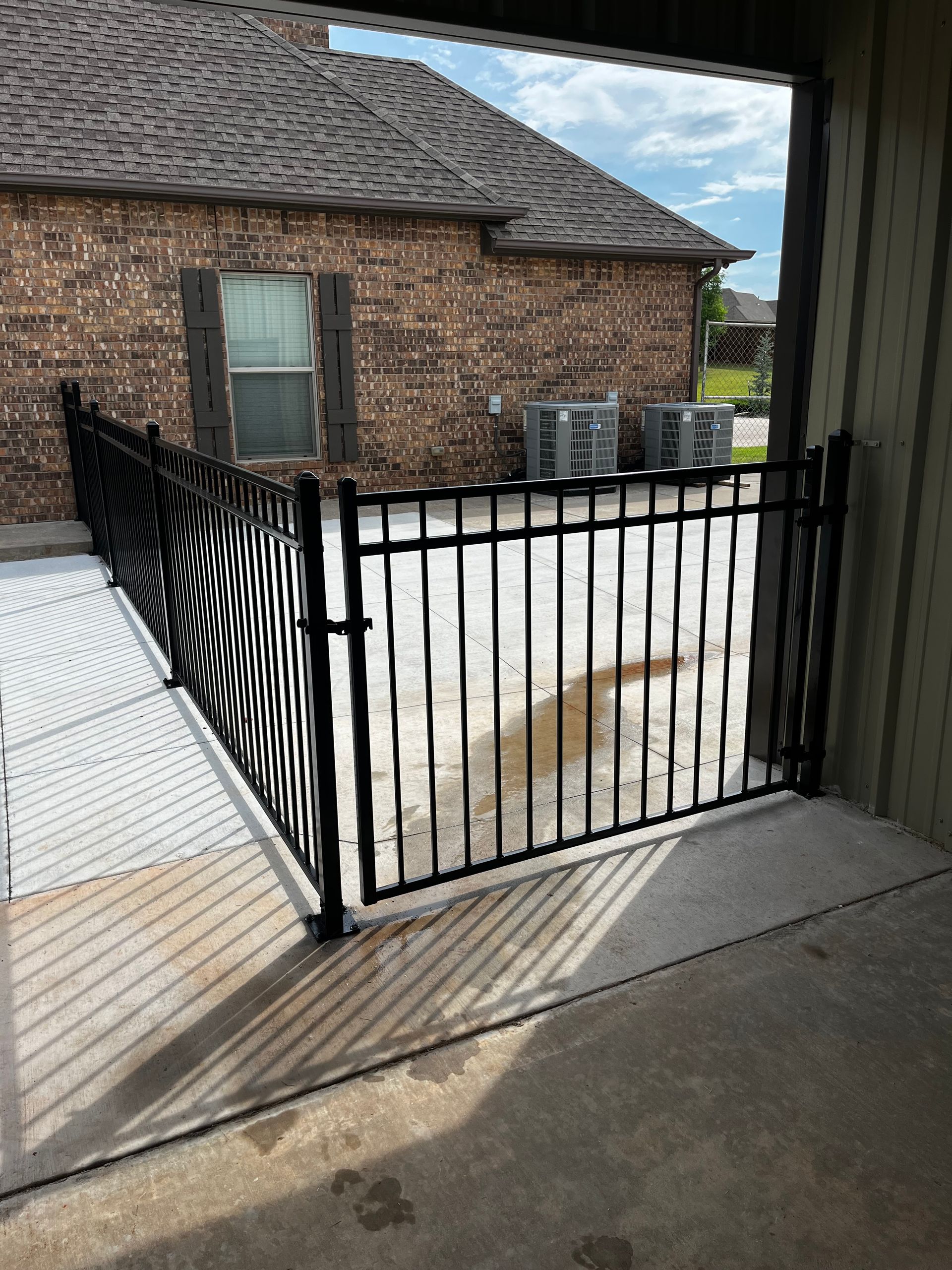 Black metal fence enclosing a concrete patio, adjacent to a brick building.