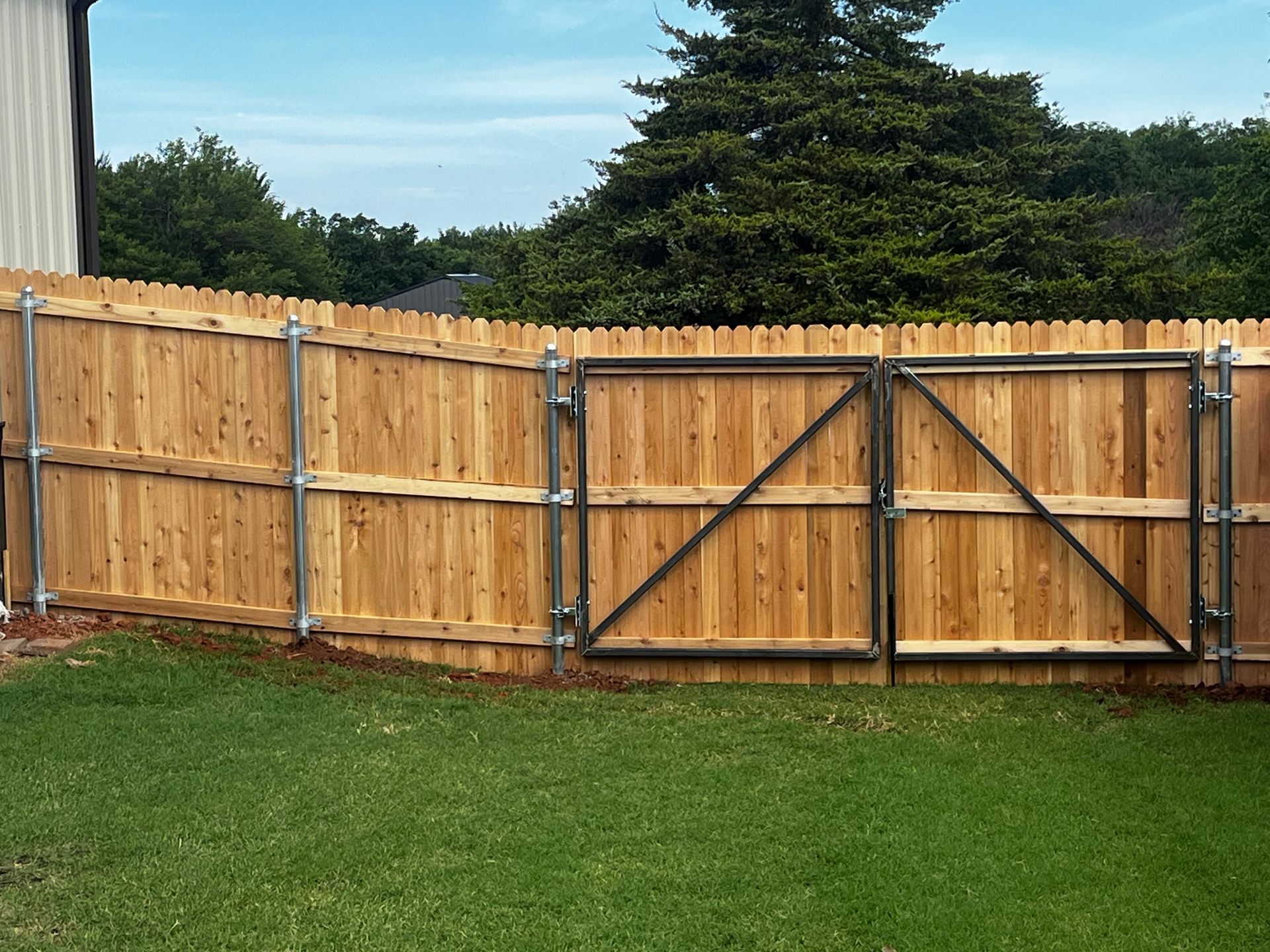 Wooden fence with metal gate in a grassy yard.
