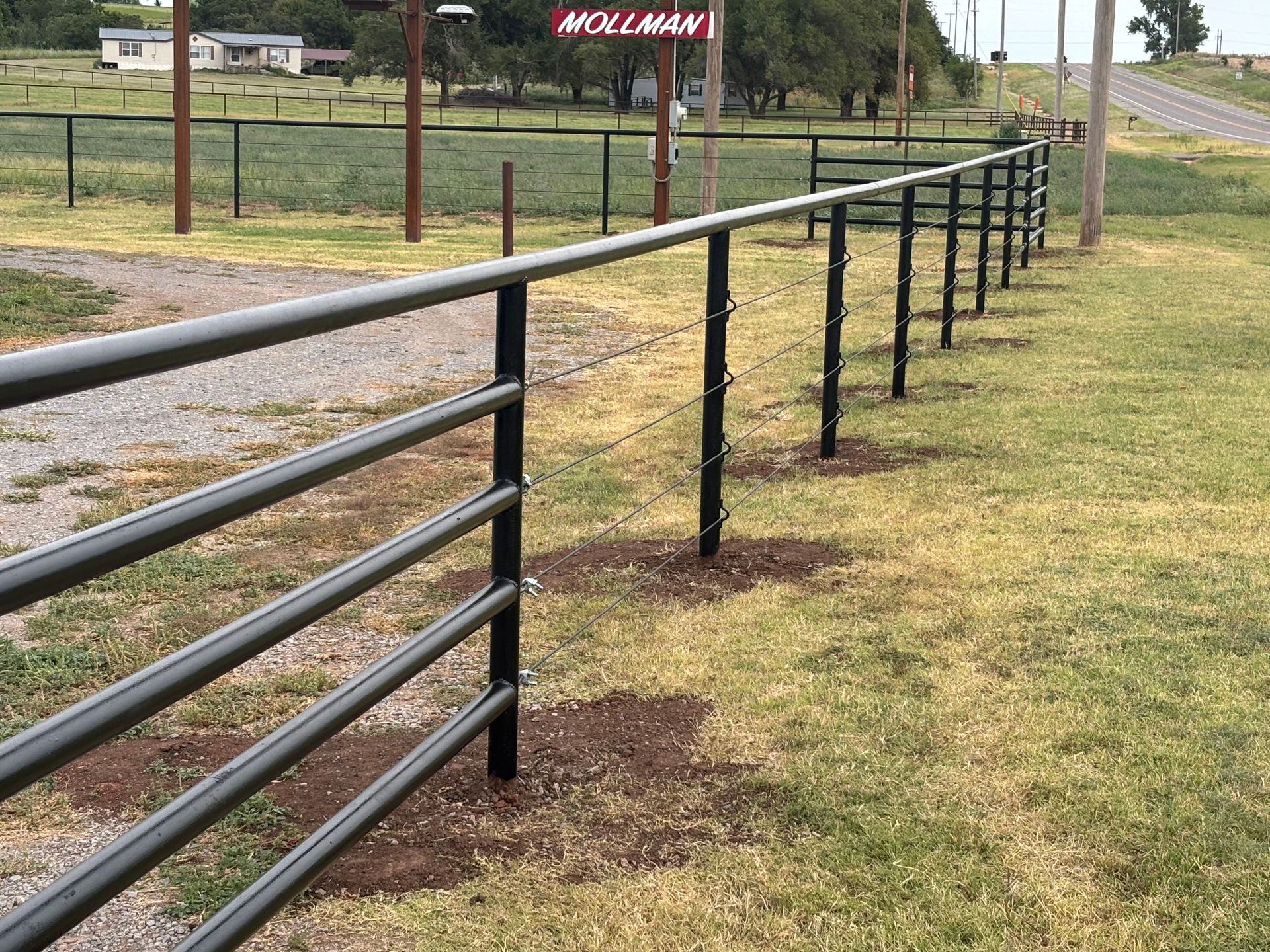 Black metal fence in a grassy field, with a gravel path to the left and a sign in the background.