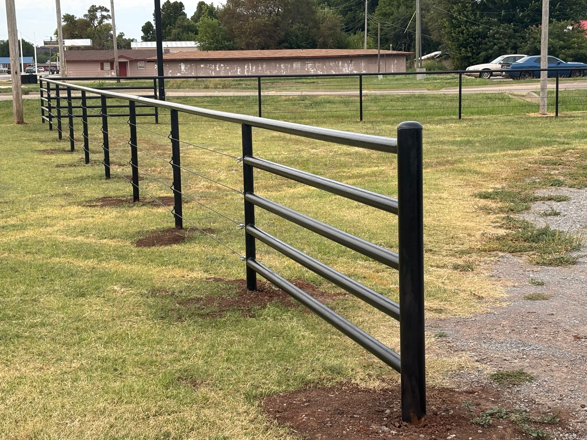 Black metal fence in a grassy field, protecting a gravel path.