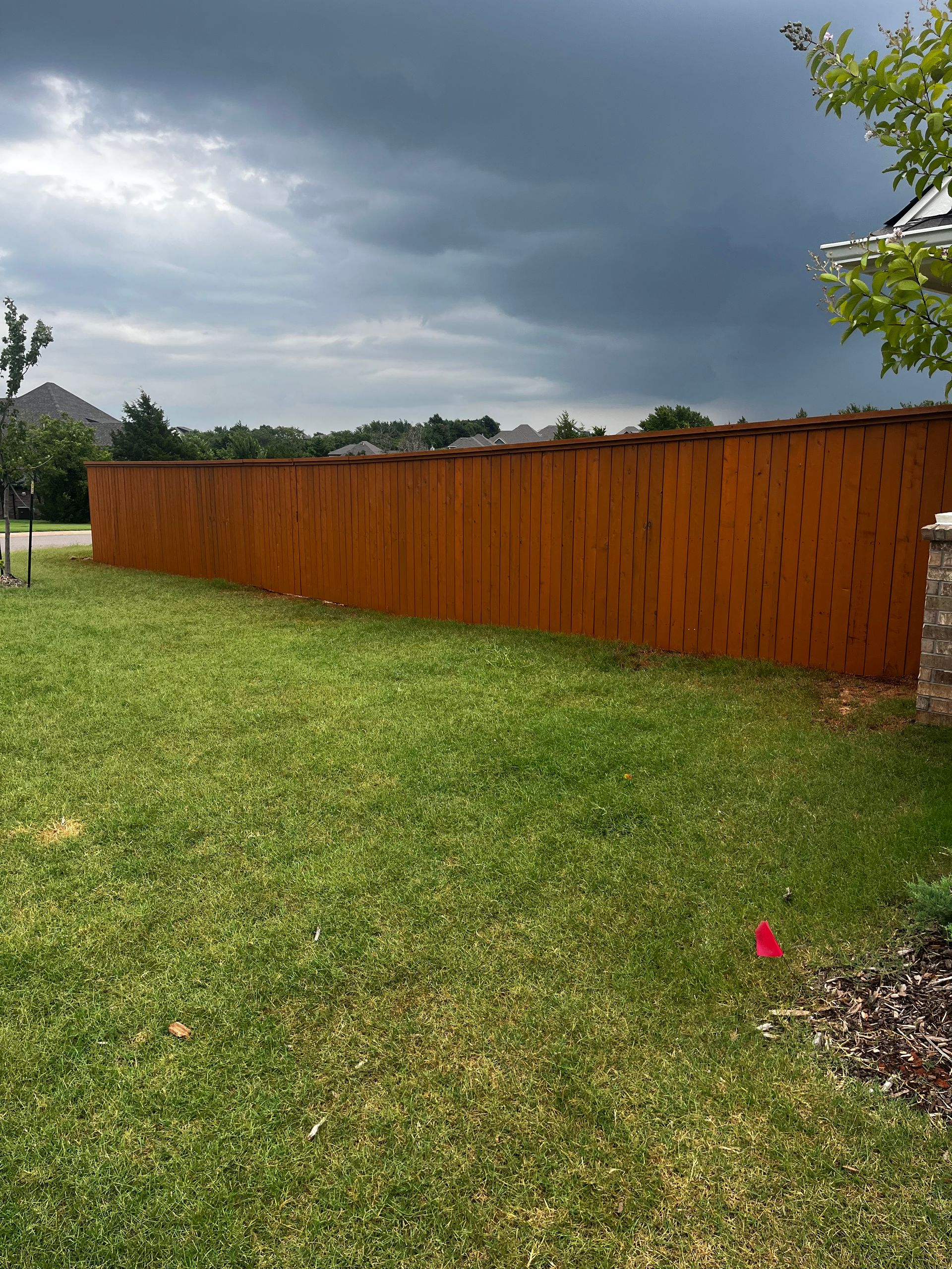 Brown wooden fence in a grassy yard under a cloudy sky.