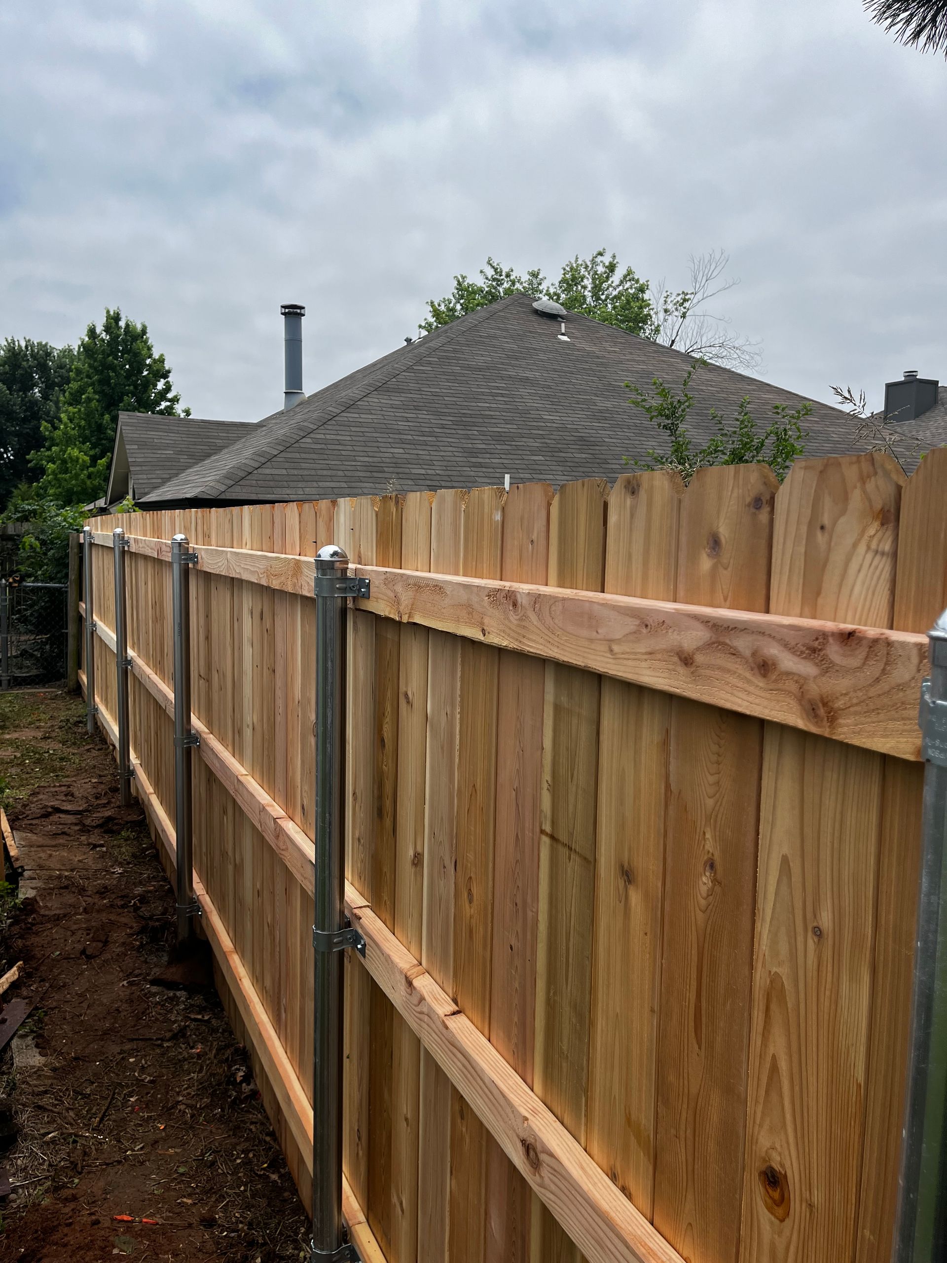 Wooden fence in a backyard setting, with a house and cloudy sky visible in the background.