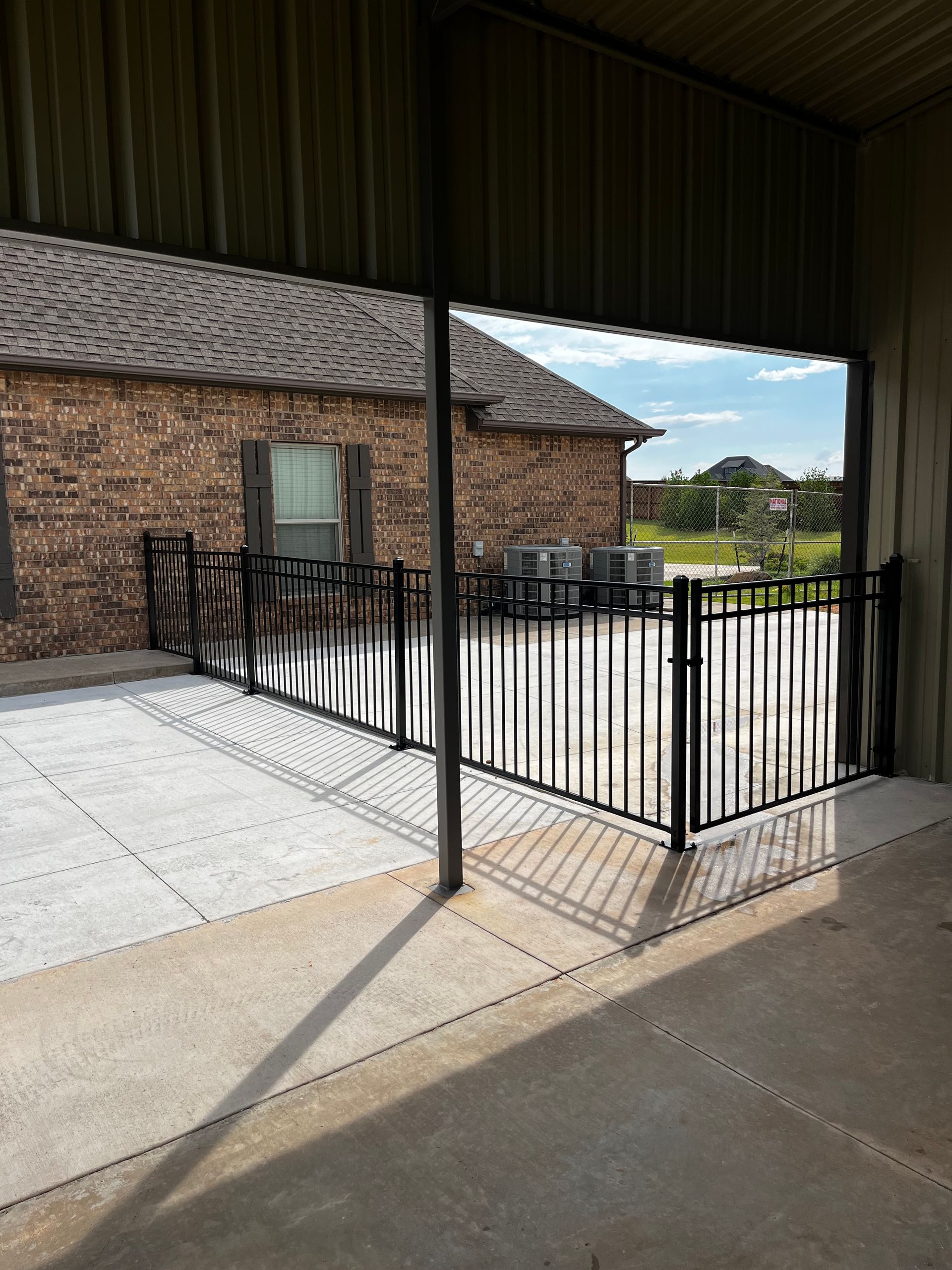 A black metal fence encloses a concrete patio beside a brick building under a covered area.